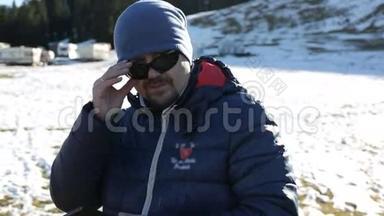 年轻有魅力的人在运动冬季服装纠正太阳镜和使用手机。